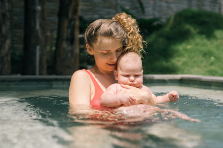 Mutter hält ihr Baby im Arm und steht im Pool.