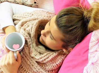 Frau liegt erkältet mit einer Tasse Tee im Bett.