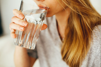 Frau hält ein Glas mit Wasser in der Hand und trinkt daraus.