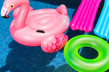 Aufblasbares Flamingo, eine rote und blaue Luftmatratze, sowie ein grüner Schwimmring schwimmen im Pool.