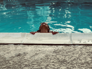 Frau stützt sich im Pool auf den Beckenrand mit den Händen
