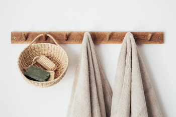Kleidehaken aus Holz an einer Wand. Es hängen zwei Handtücher und ein Korb mit Wellness Zubehör daran.