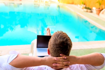 Mann entspannt mit Laptop vor einem Pool